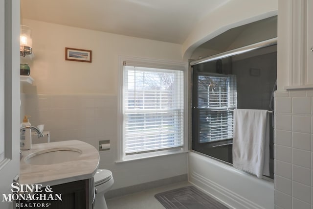 full bathroom featuring bath / shower combo with glass door, tile walls, vanity, and toilet