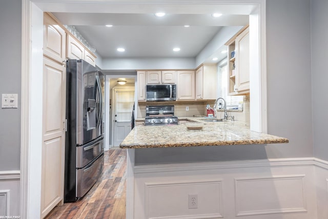 kitchen with sink, appliances with stainless steel finishes, light stone countertops, dark hardwood / wood-style flooring, and kitchen peninsula