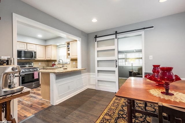 kitchen with appliances with stainless steel finishes, backsplash, dark hardwood / wood-style floors, light stone counters, and a barn door