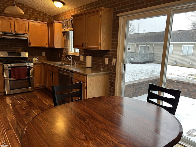 kitchen with range with two ovens, brown cabinetry, dark wood-type flooring, under cabinet range hood, and a sink