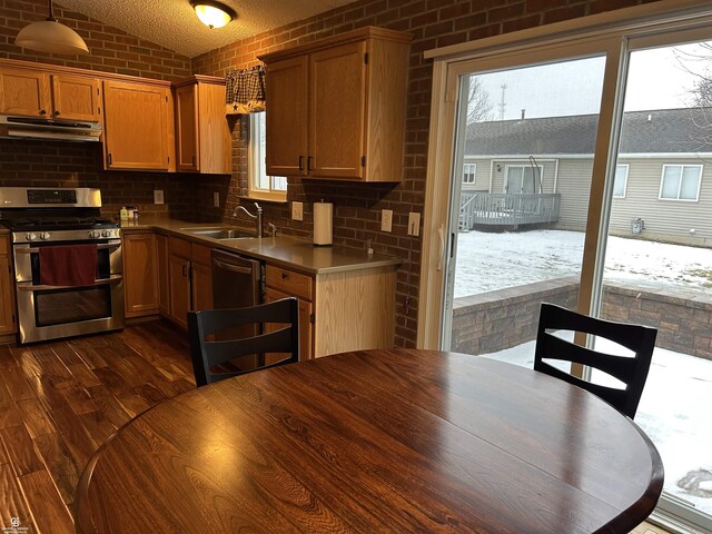 kitchen with dark wood finished floors, brown cabinets, under cabinet range hood, double oven range, and a sink