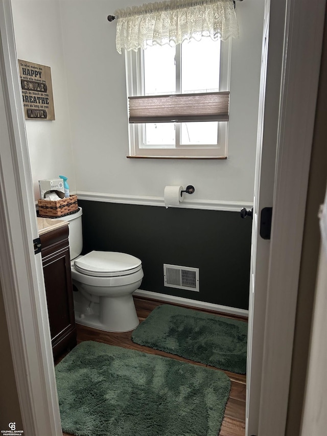 half bath featuring toilet, wood finished floors, vanity, and visible vents