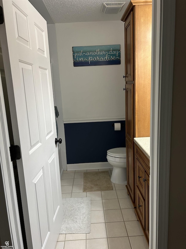 bathroom featuring visible vents, toilet, vanity, a textured ceiling, and tile patterned flooring