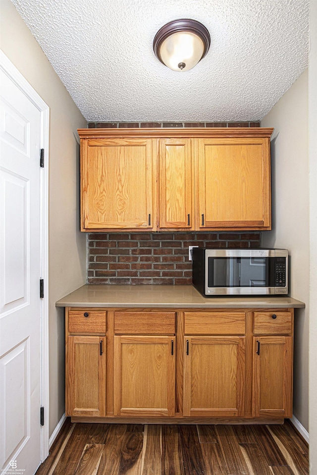 kitchen featuring light countertops, dark wood-style flooring, stainless steel microwave, and a textured ceiling