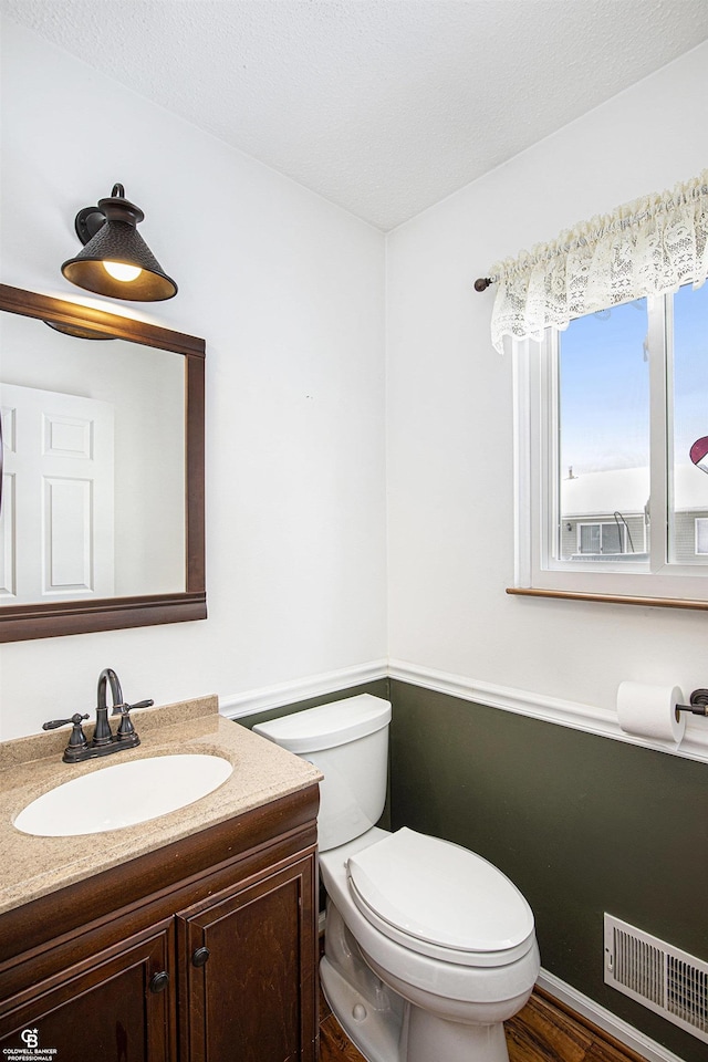 half bath featuring toilet, a textured ceiling, vanity, and visible vents