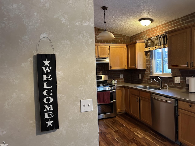 kitchen featuring dark wood-style floors, stainless steel appliances, hanging light fixtures, a sink, and a textured ceiling