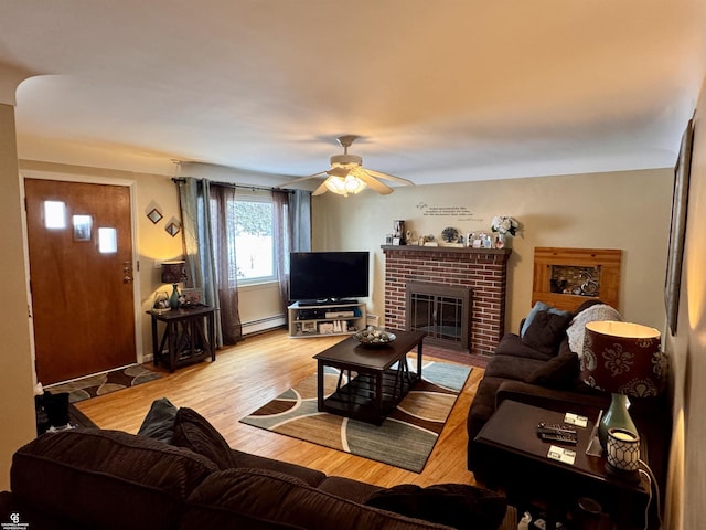 living room with a baseboard heating unit, ceiling fan, a brick fireplace, and light wood-type flooring