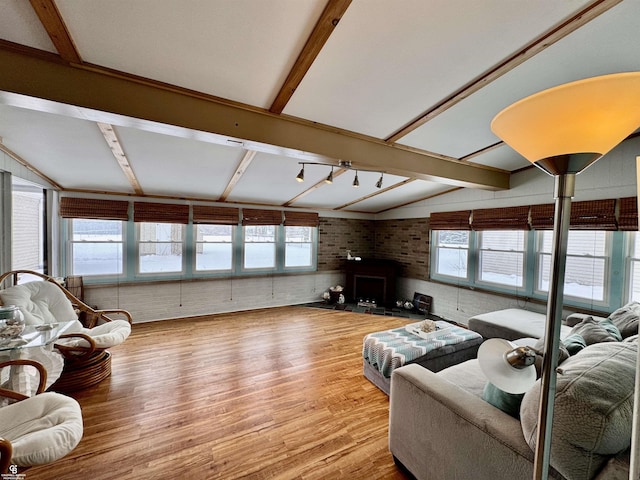 living room featuring brick wall, vaulted ceiling with beams, hardwood / wood-style floors, and a fireplace