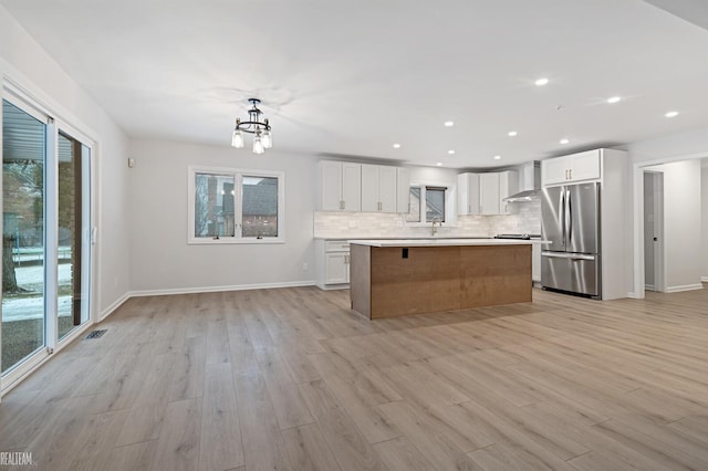 kitchen featuring white cabinets, a center island, stainless steel fridge, and wall chimney exhaust hood