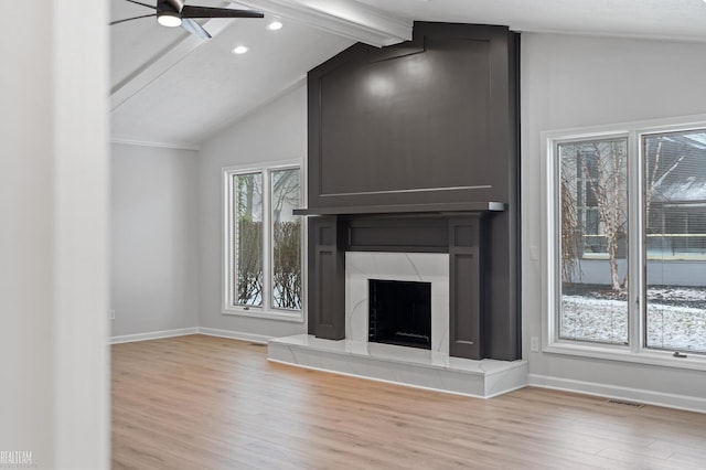 unfurnished living room featuring ceiling fan, a large fireplace, light hardwood / wood-style flooring, and vaulted ceiling with beams