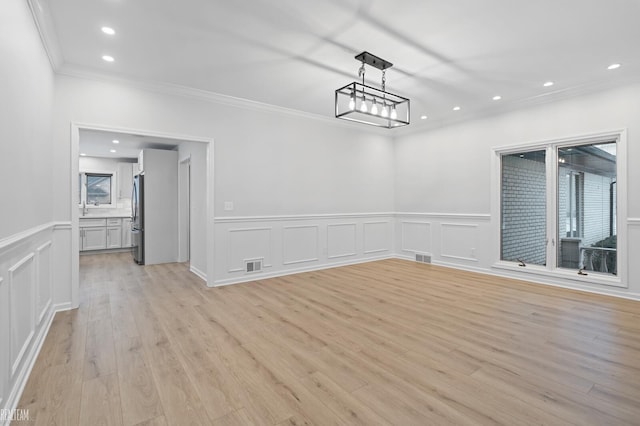 unfurnished dining area with crown molding, plenty of natural light, a chandelier, and light hardwood / wood-style flooring