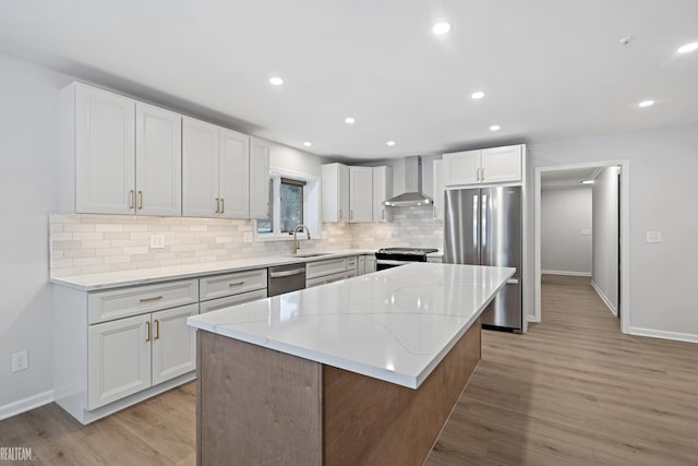 kitchen with appliances with stainless steel finishes, white cabinetry, sink, a center island, and wall chimney exhaust hood