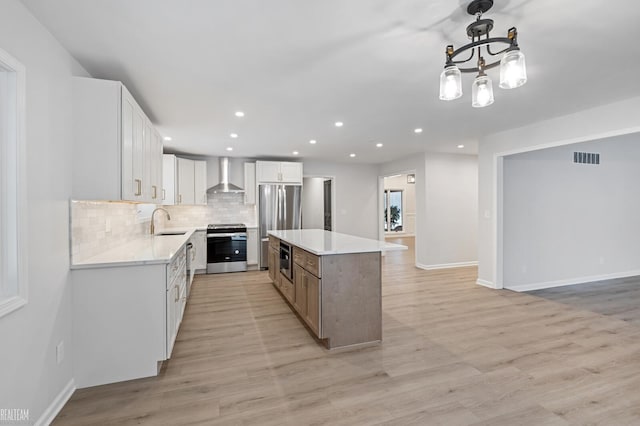 kitchen featuring wall chimney exhaust hood, white cabinetry, hanging light fixtures, a kitchen island, and stainless steel appliances