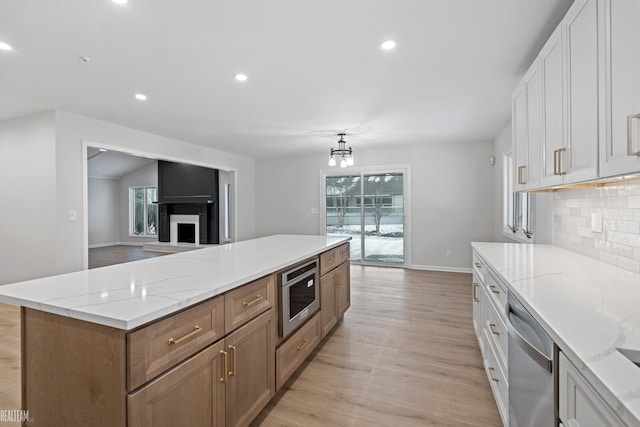 kitchen with light stone counters, light hardwood / wood-style floors, white cabinets, decorative backsplash, and stainless steel dishwasher