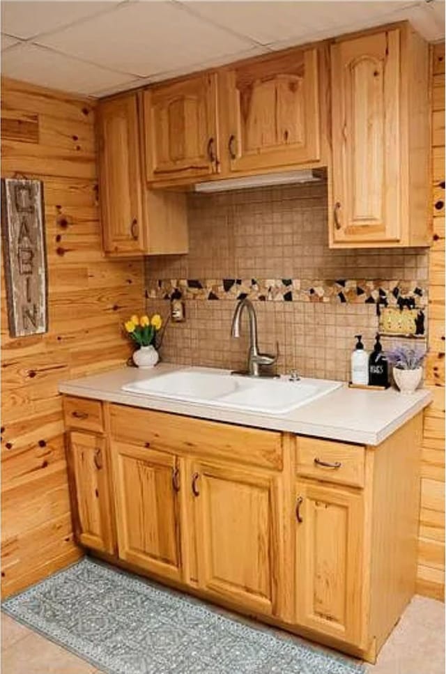 kitchen featuring tasteful backsplash, sink, light tile patterned floors, and wooden walls