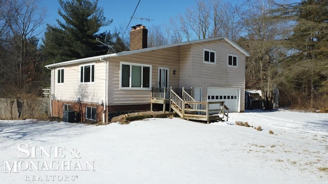 snow covered back of property featuring a garage and central air condition unit