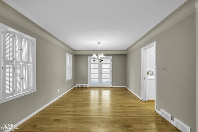 unfurnished dining area with crown molding, hardwood / wood-style floors, a notable chandelier, and a wealth of natural light