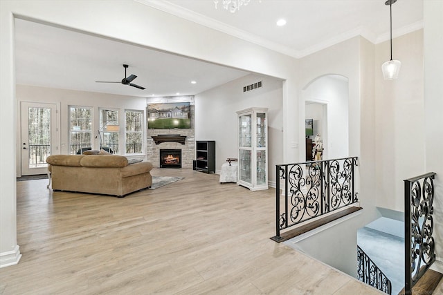 living room with crown molding, a fireplace, ceiling fan, and light wood-type flooring