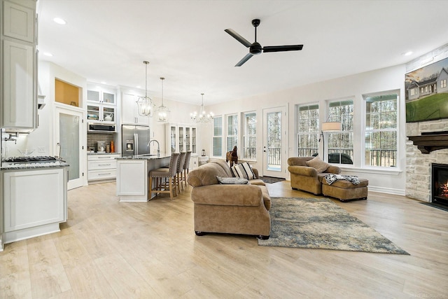 living room featuring sink, ceiling fan with notable chandelier, a fireplace, and light hardwood / wood-style floors