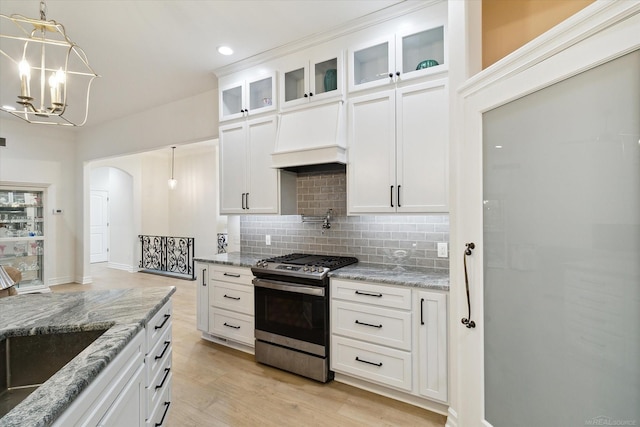 kitchen featuring custom exhaust hood, stainless steel gas range, hanging light fixtures, and white cabinets