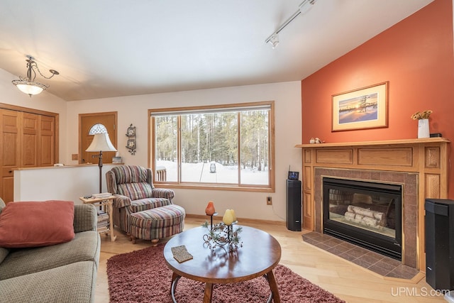 living room with track lighting, a fireplace, light hardwood / wood-style floors, and vaulted ceiling