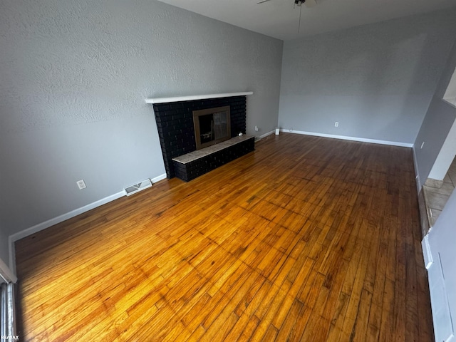 unfurnished living room featuring ceiling fan, wood-type flooring, and a fireplace