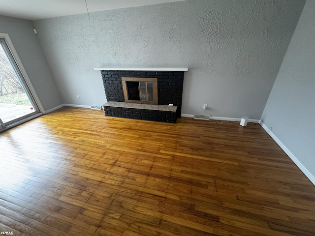 unfurnished living room with wood-type flooring and a brick fireplace