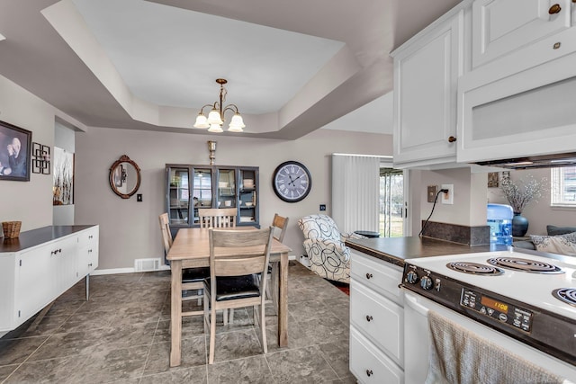 kitchen with white cabinetry, a chandelier, hanging light fixtures, a tray ceiling, and white appliances