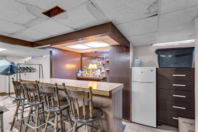 bar featuring white fridge, dark brown cabinets, a paneled ceiling, and wooden walls