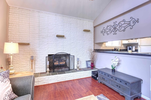 living room with sink, dark wood-type flooring, a brick fireplace, and vaulted ceiling