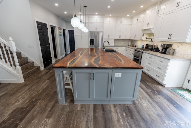 kitchen featuring white cabinetry, stainless steel appliances, butcher block countertops, and a large island with sink