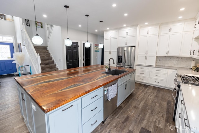 kitchen with sink, wooden counters, decorative light fixtures, stainless steel appliances, and a kitchen island with sink