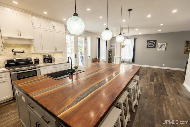 kitchen featuring stainless steel gas stove, sink, wooden counters, white cabinets, and hanging light fixtures