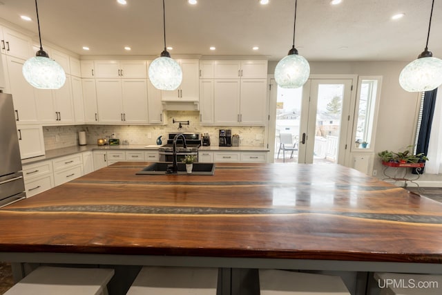 kitchen with wooden counters, a center island with sink, white cabinets, and decorative light fixtures