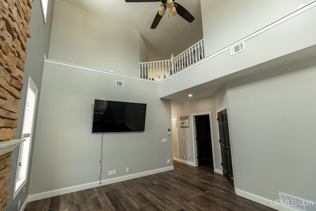 unfurnished living room with dark wood-type flooring, ceiling fan, and a high ceiling