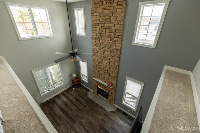 living room featuring dark hardwood / wood-style floors, ceiling fan, a fireplace, and a high ceiling