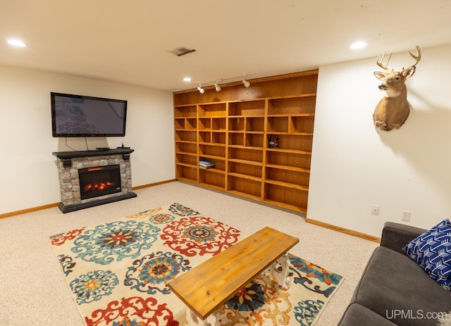 living room with a stone fireplace, carpet floors, and rail lighting