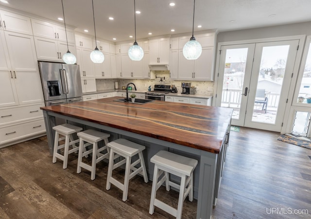 kitchen with stainless steel appliances, a kitchen island with sink, and butcher block countertops