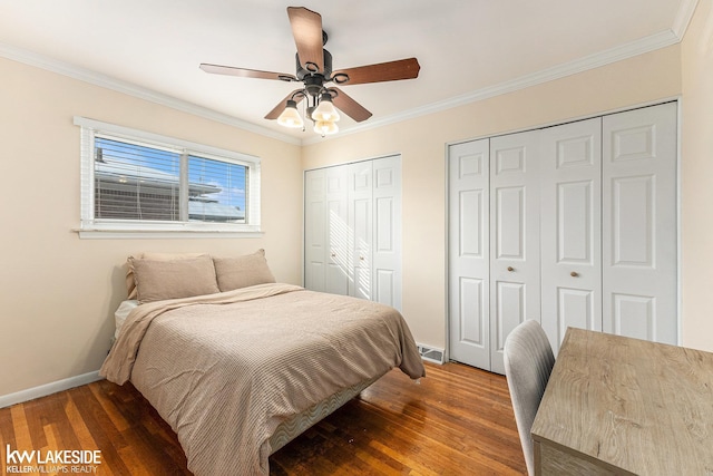 bedroom with dark hardwood / wood-style flooring, two closets, crown molding, and ceiling fan