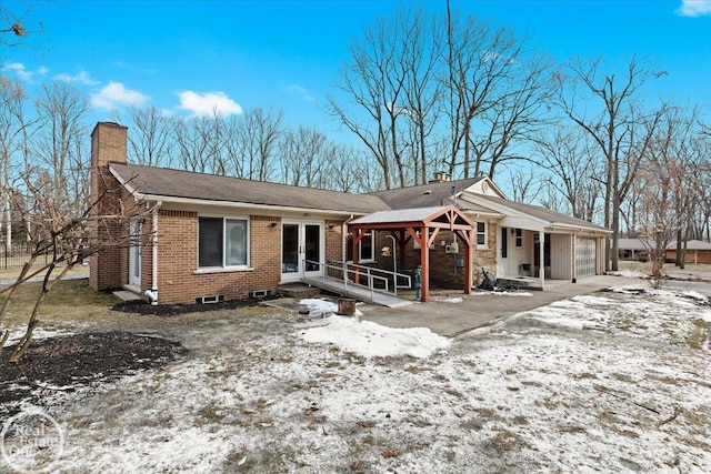 snow covered rear of property featuring a garage and french doors