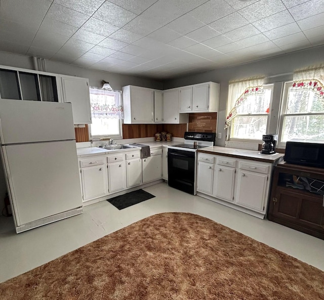 kitchen featuring white refrigerator, white cabinetry, sink, and electric range