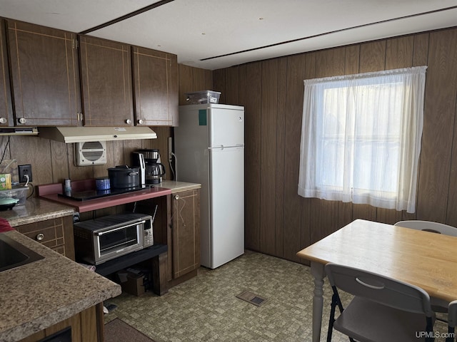 kitchen with dark brown cabinets, wooden walls, and white fridge