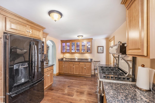 kitchen featuring black fridge, dark stone countertops, dark hardwood / wood-style flooring, and stainless steel gas range oven