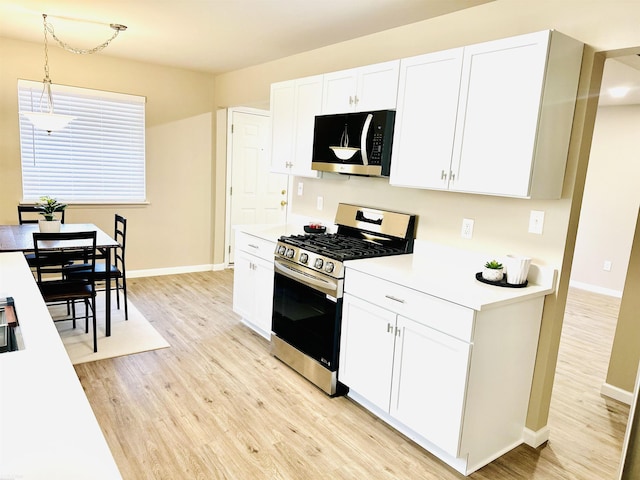 kitchen with white cabinetry, stainless steel appliances, decorative light fixtures, and light hardwood / wood-style flooring