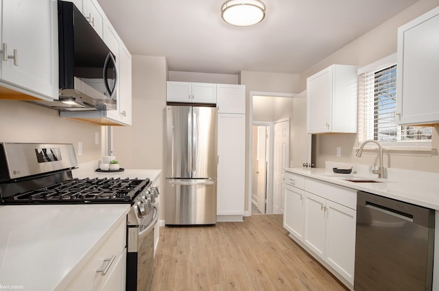 kitchen with appliances with stainless steel finishes, sink, white cabinets, and light hardwood / wood-style flooring