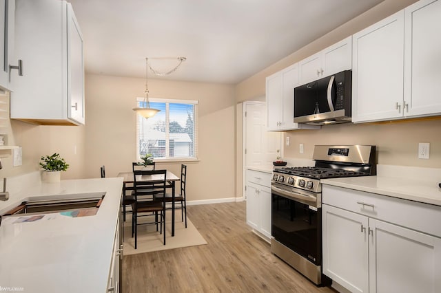 kitchen with stainless steel range with gas stovetop, sink, hanging light fixtures, and white cabinets