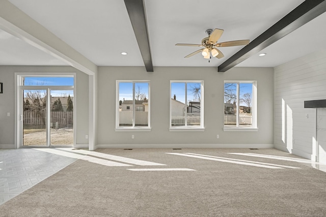 unfurnished living room featuring beamed ceiling, ceiling fan, plenty of natural light, and light carpet