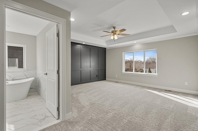 unfurnished bedroom with ceiling fan, a raised ceiling, light carpet, and a closet