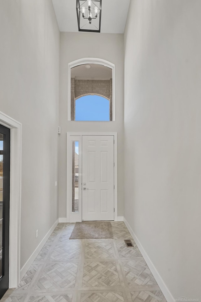 foyer with a high ceiling, light parquet floors, and a notable chandelier