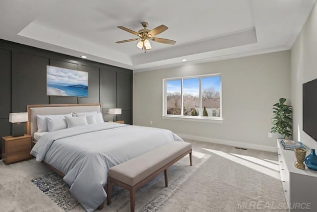 bedroom with light carpet, a tray ceiling, and ceiling fan